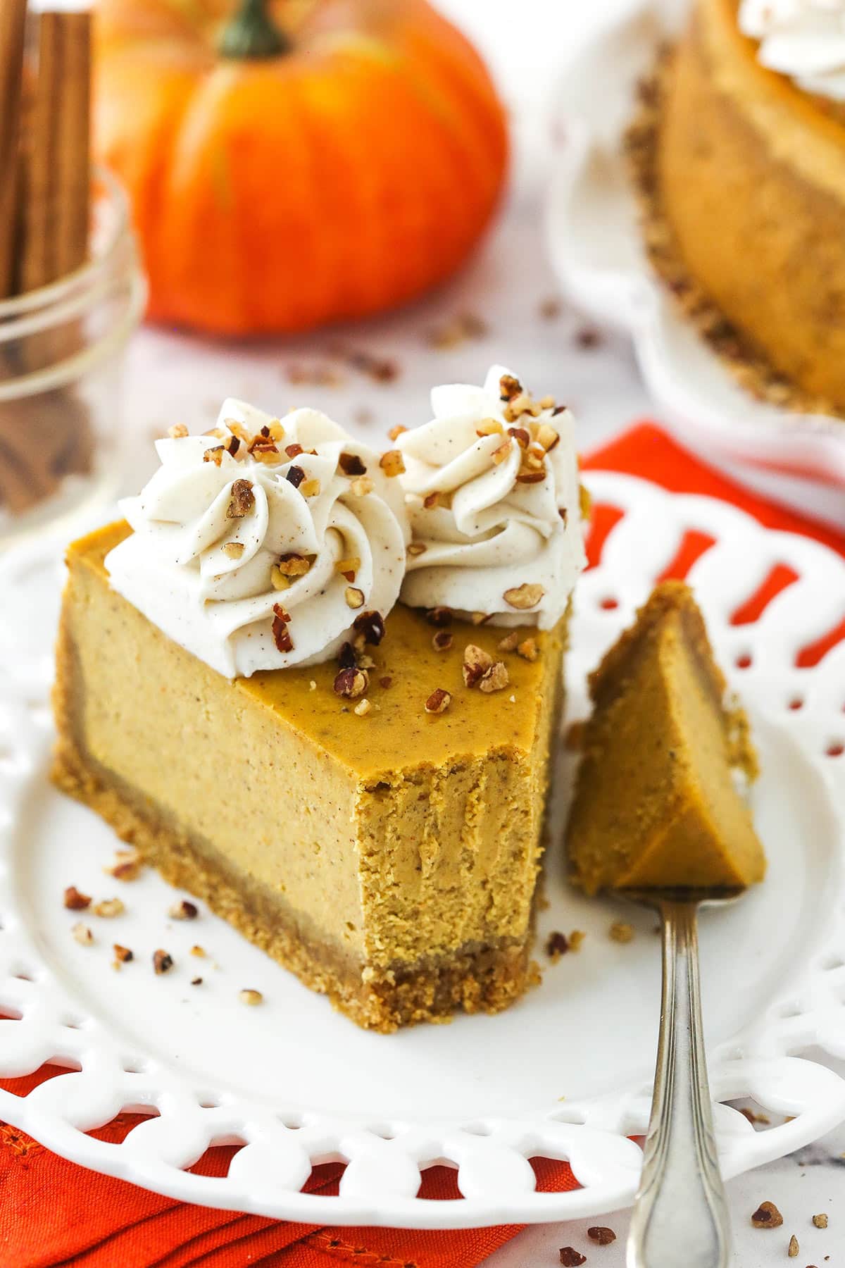 A piece of pumpkin cheesecake on a plate with one bite on a metal fork