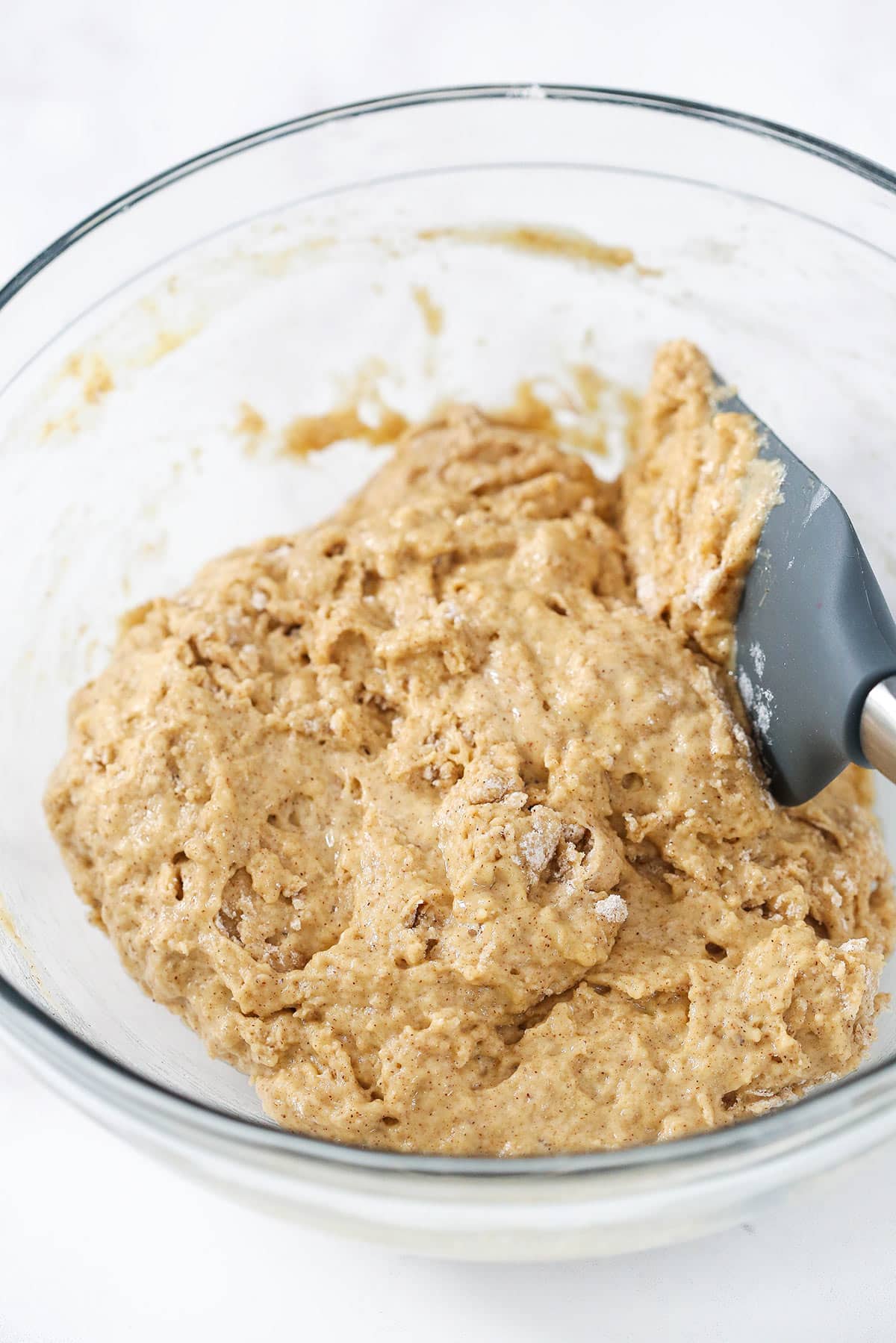 The mostly combined wet and dry ingredients inside of a big clear mixing bowl