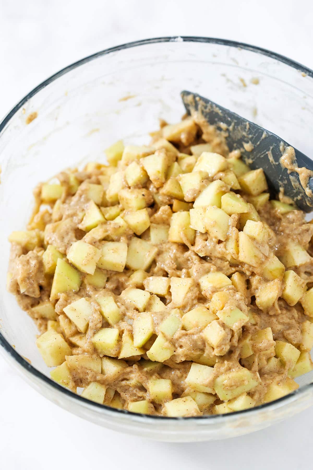 Chopped apples and butter being folded into the fritter batter with a rubber spatula
