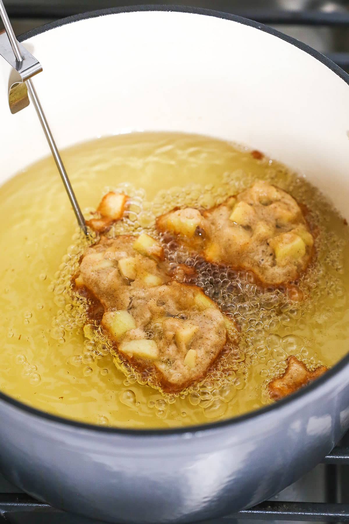 Two half-cooked apple fritters frying in boiling vegetable oil