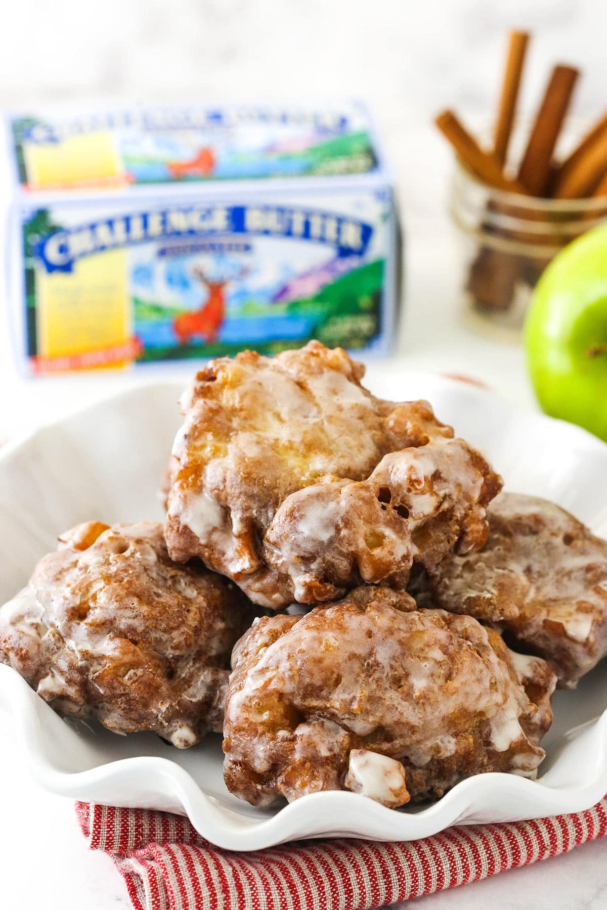 A plate of five apple fritters with butter and cinnamon sticks behind it