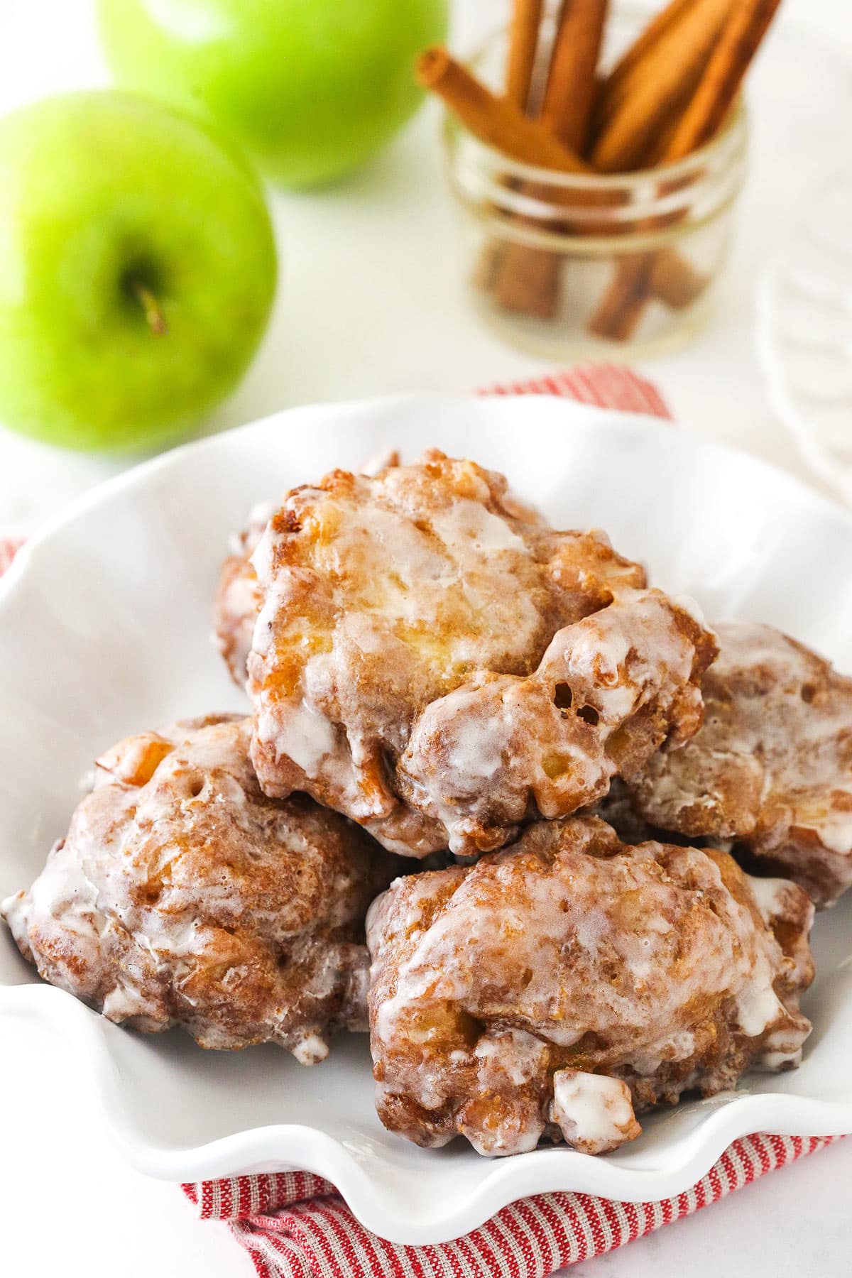 Five homemade apple fritters coated in vanilla glaze on a marble countertop