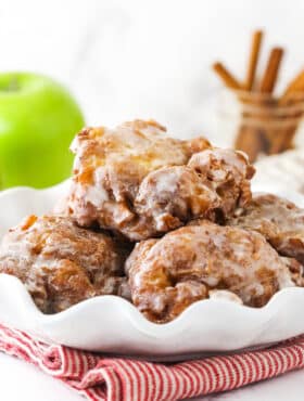 A white serving platter holding a pile of homemade apple fritters
