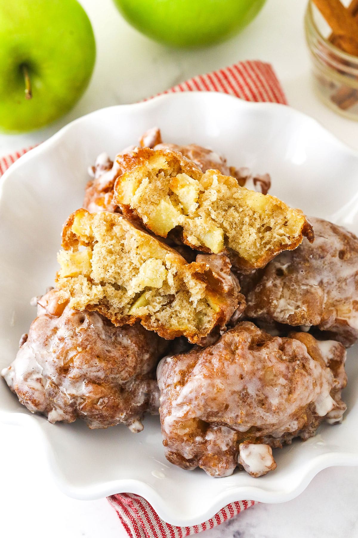 Fresh apple fritters in a fancy white bowl with one broken in half to show the fluffy interior