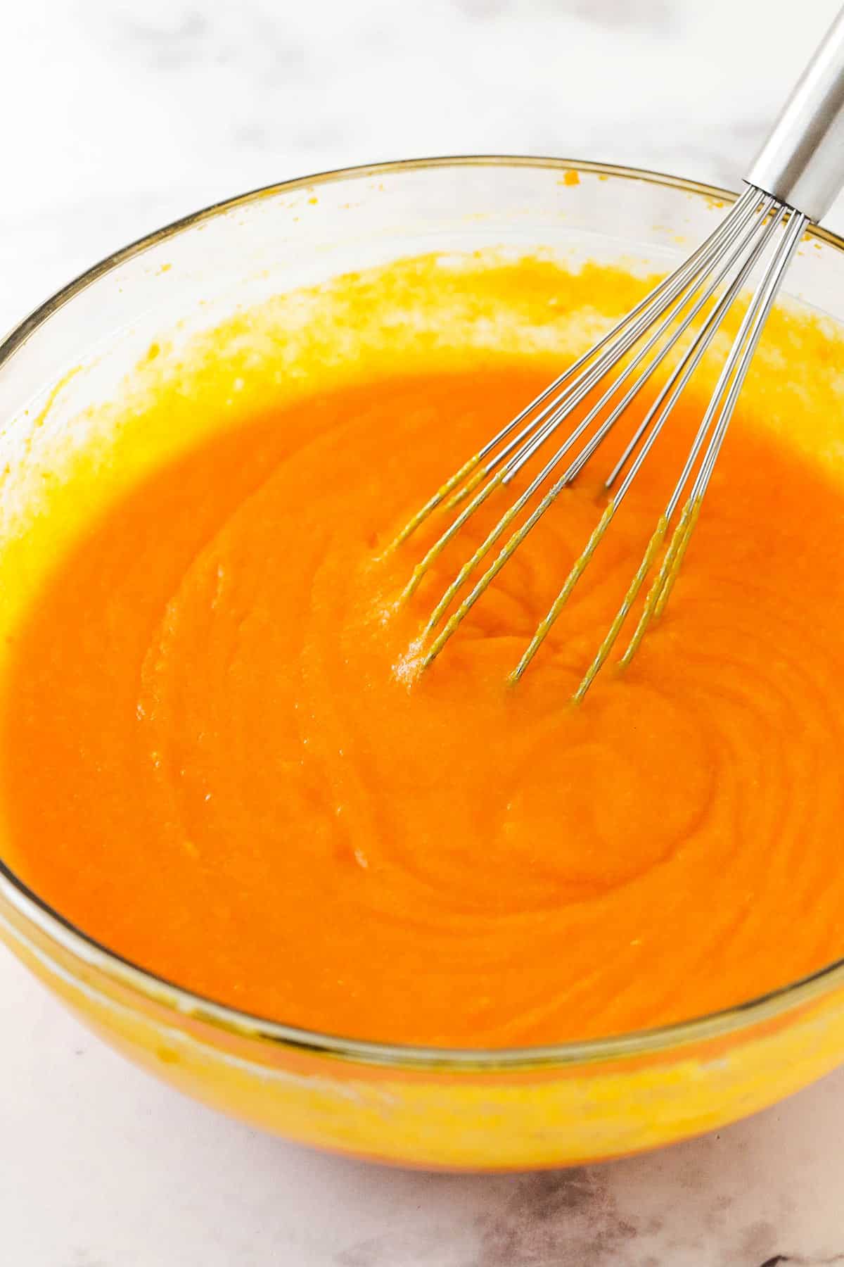 A metal whisk being used to mix the batter in a large glass bowl