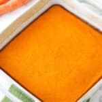 A freshly baked carrot souffle inside of a white baking dish with handles