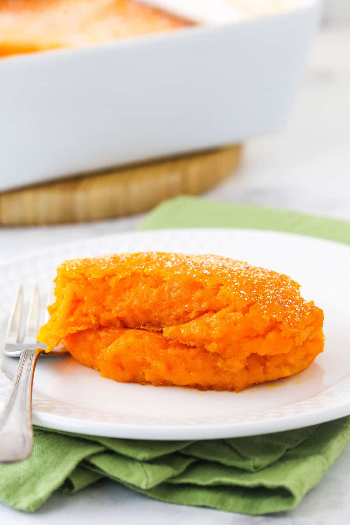 A serving of carrot souffle on a white plate with a fork beside it