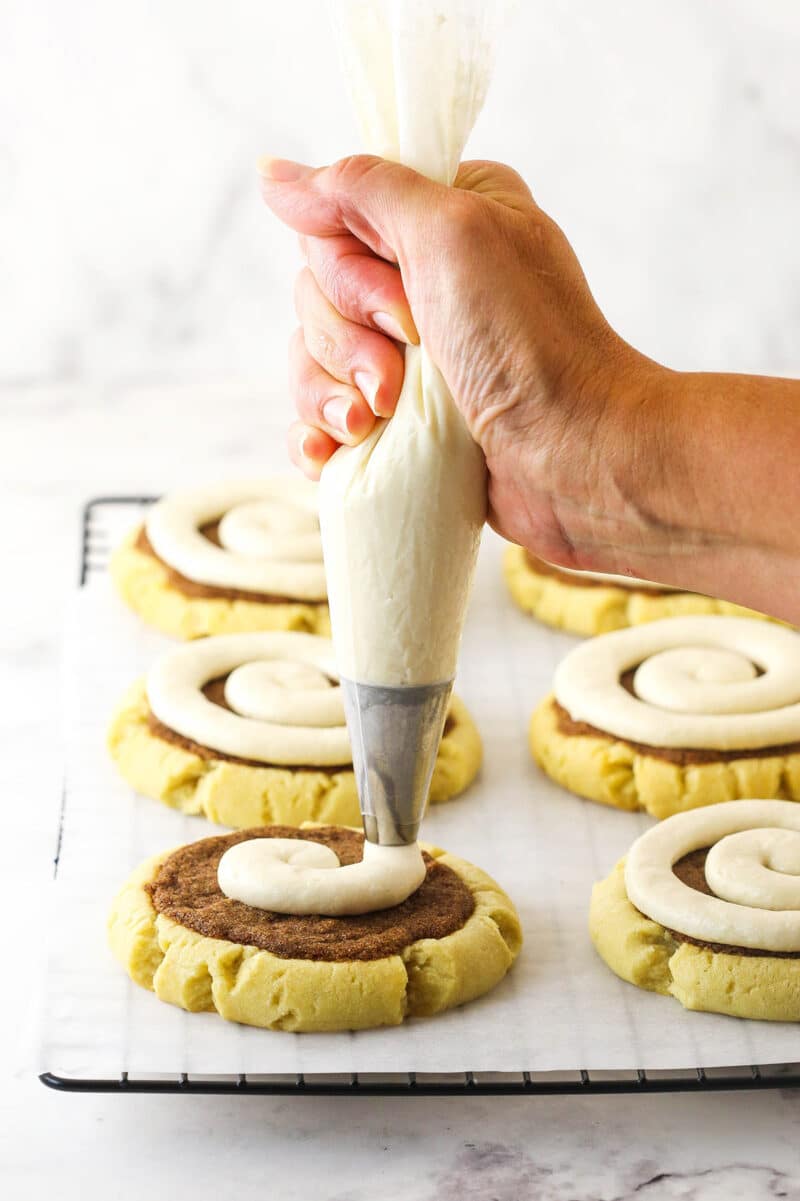 Maple buttercream being piped onto a cinnamon roll cookie in a swirl pattern