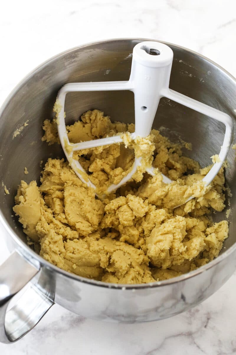 The sugar cookie dough being combined in a metal mixing bowl