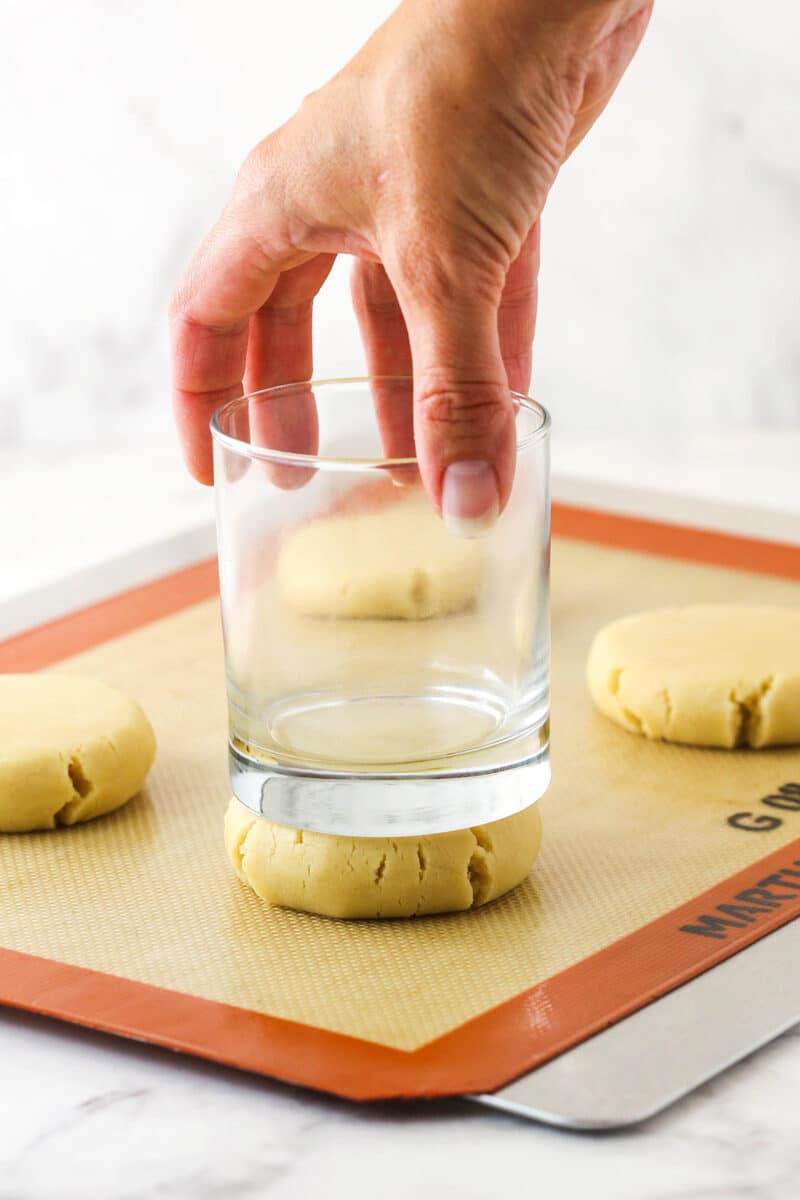 A short glass being used to gently flatten a ball of cookie dough