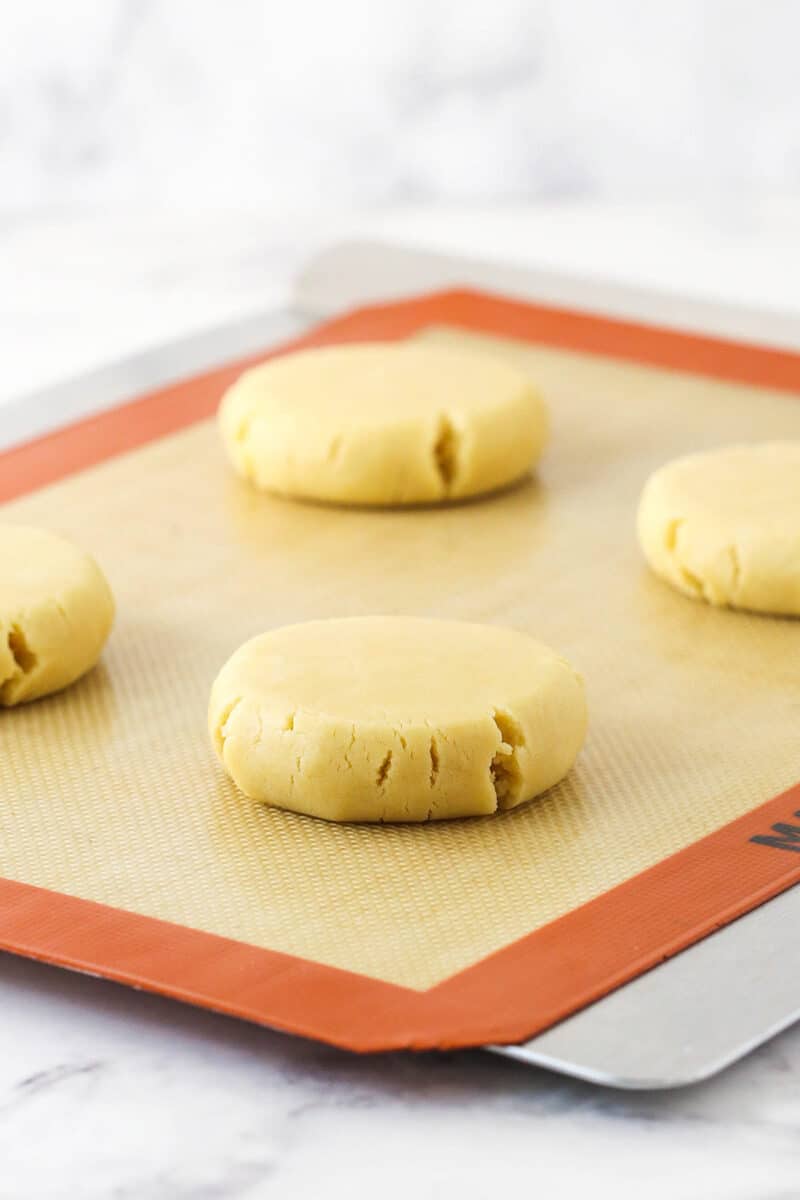 Discs of sugar cookie dough on a baking sheet lined with a silicone baking mat