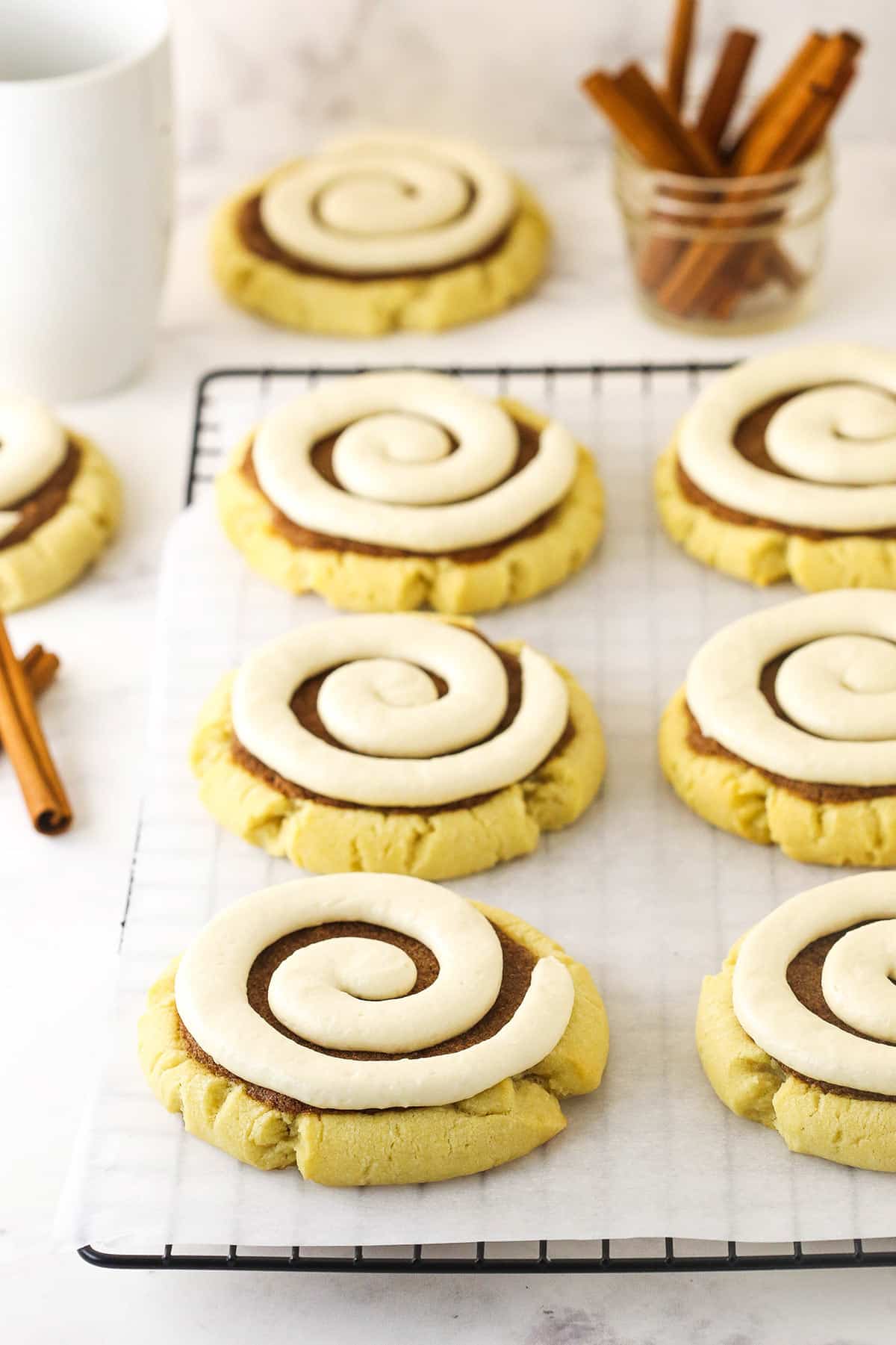 A batch of copycat Crumbl cinnamon roll cookies on a kitchen countertop with a jar full of cinnamon sticks