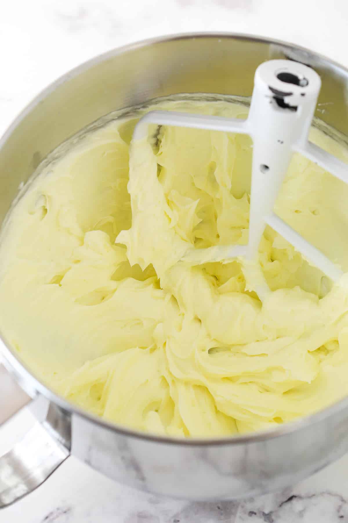 A metal mixing bowl full of creamed butter and cream cheese