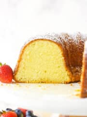 About half of a cream cheese pound cake on a wooden cake stand with a plastic platform