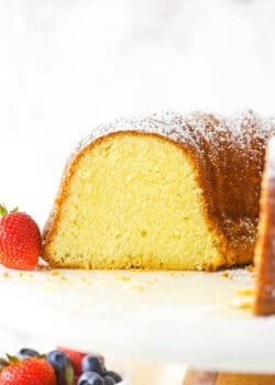 About half of a cream cheese pound cake on a wooden cake stand with a plastic platform