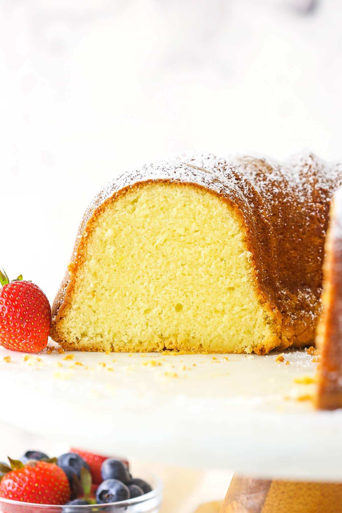 About half of a cream cheese pound cake on a wooden cake stand with a plastic platform