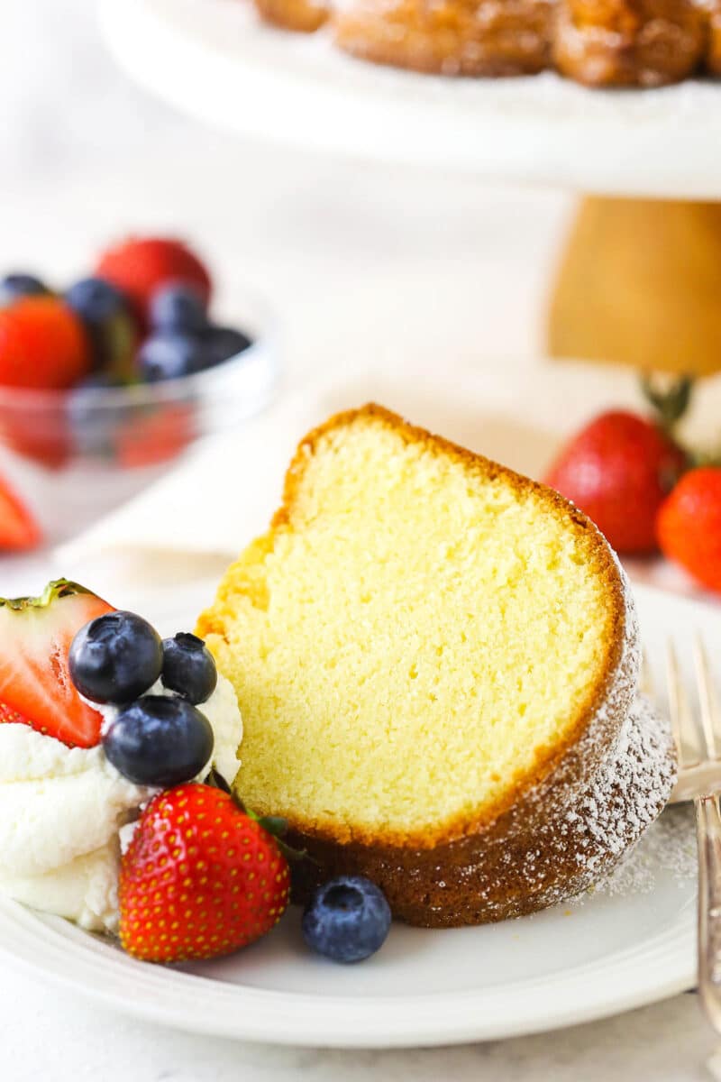 A serving of bundt cake on a dessert plate with a bowl of strawberries and blueberries behind it