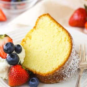 A slice of pound cake on a small plate with fresh berries and whipped cream