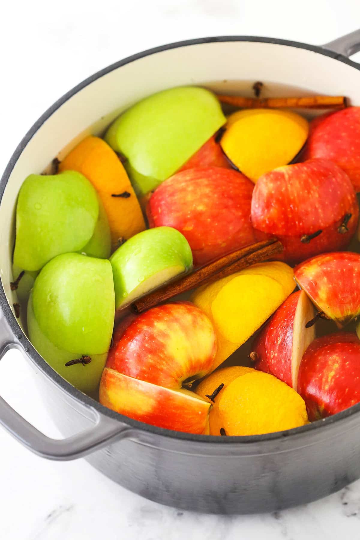 Quartered apples in a stockpot with a quartered orange, cloves and cinnamon sticks