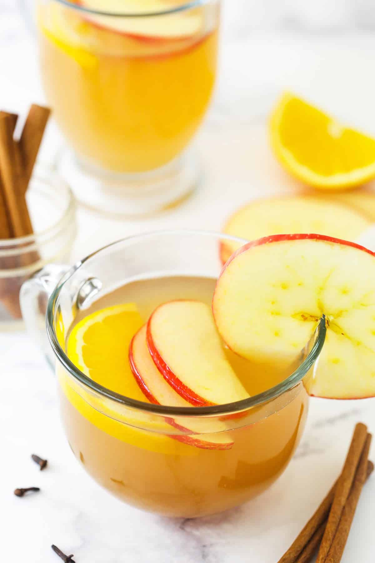 A clear mug full of mulled apple cider on a marble kitchen countertop