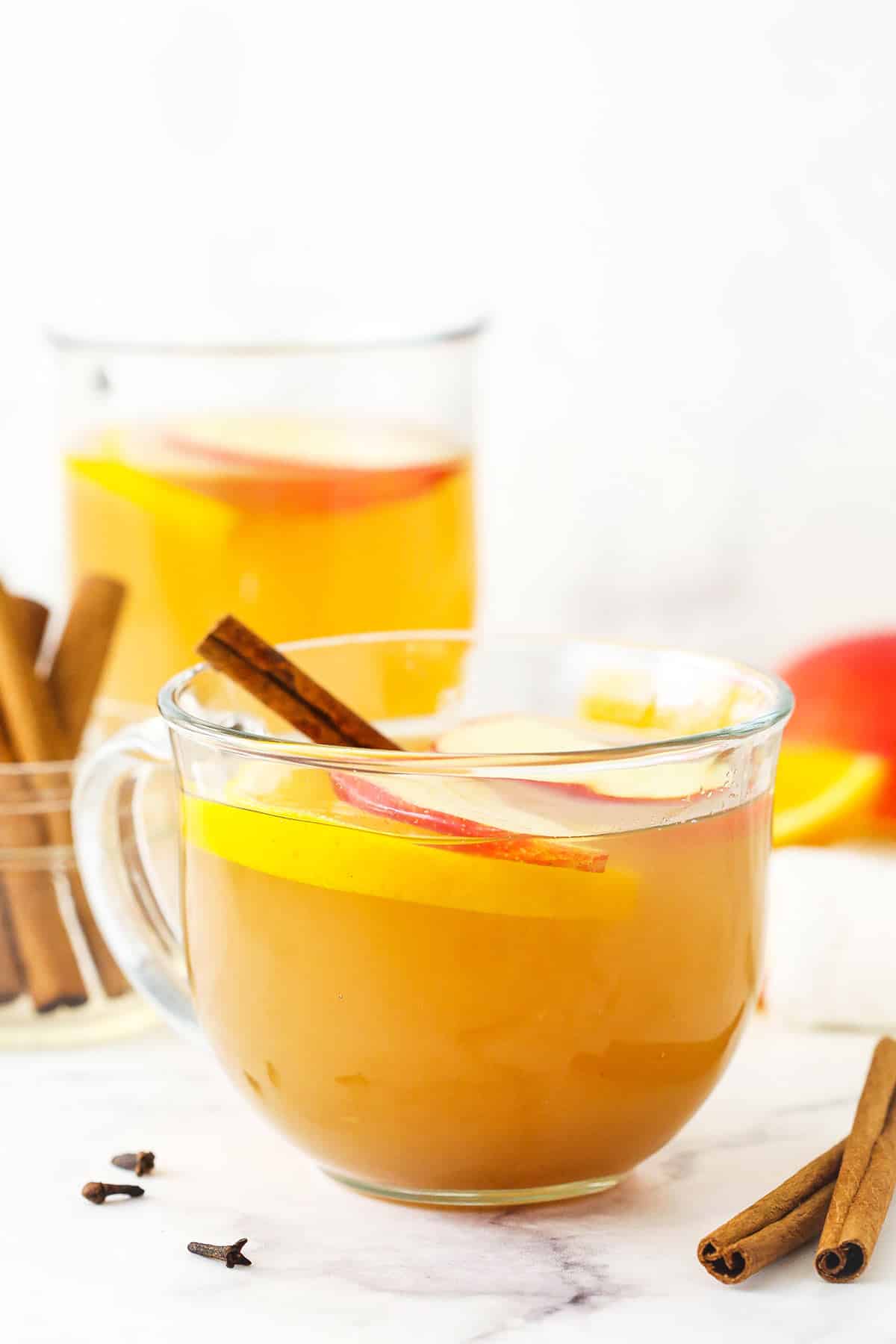 Homemade apple cider in a mug with a cinnamon stick, an orange slice and two apple slices on top as a garnish