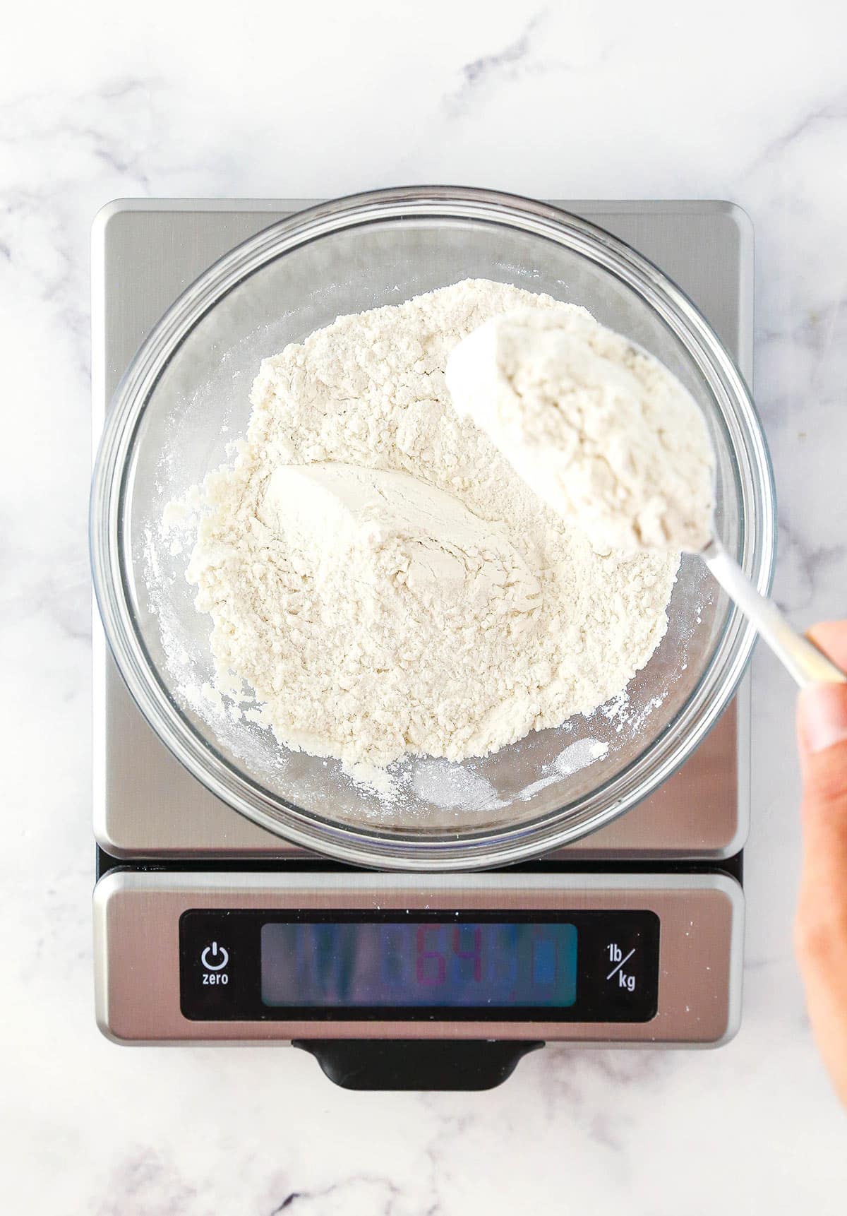 A bowl full of flour on a kitchen scale on top of a marble counter