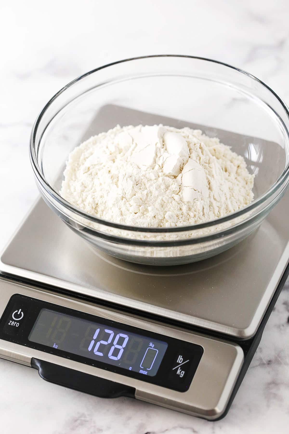 A bowl of flour on a kitchen scale that says 128 grams