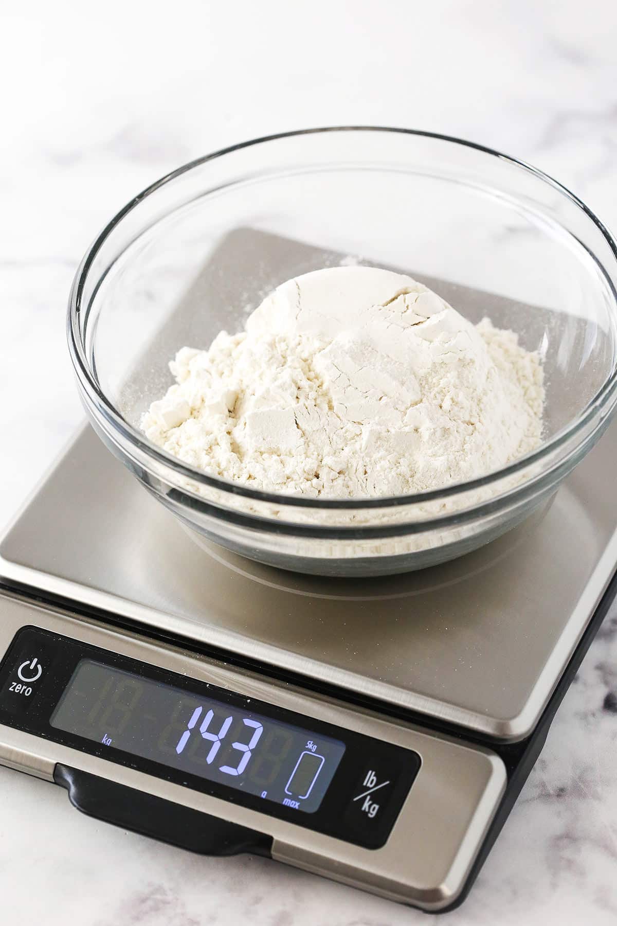 Flour in a bowl on a food scale with the screen reading 143 grams