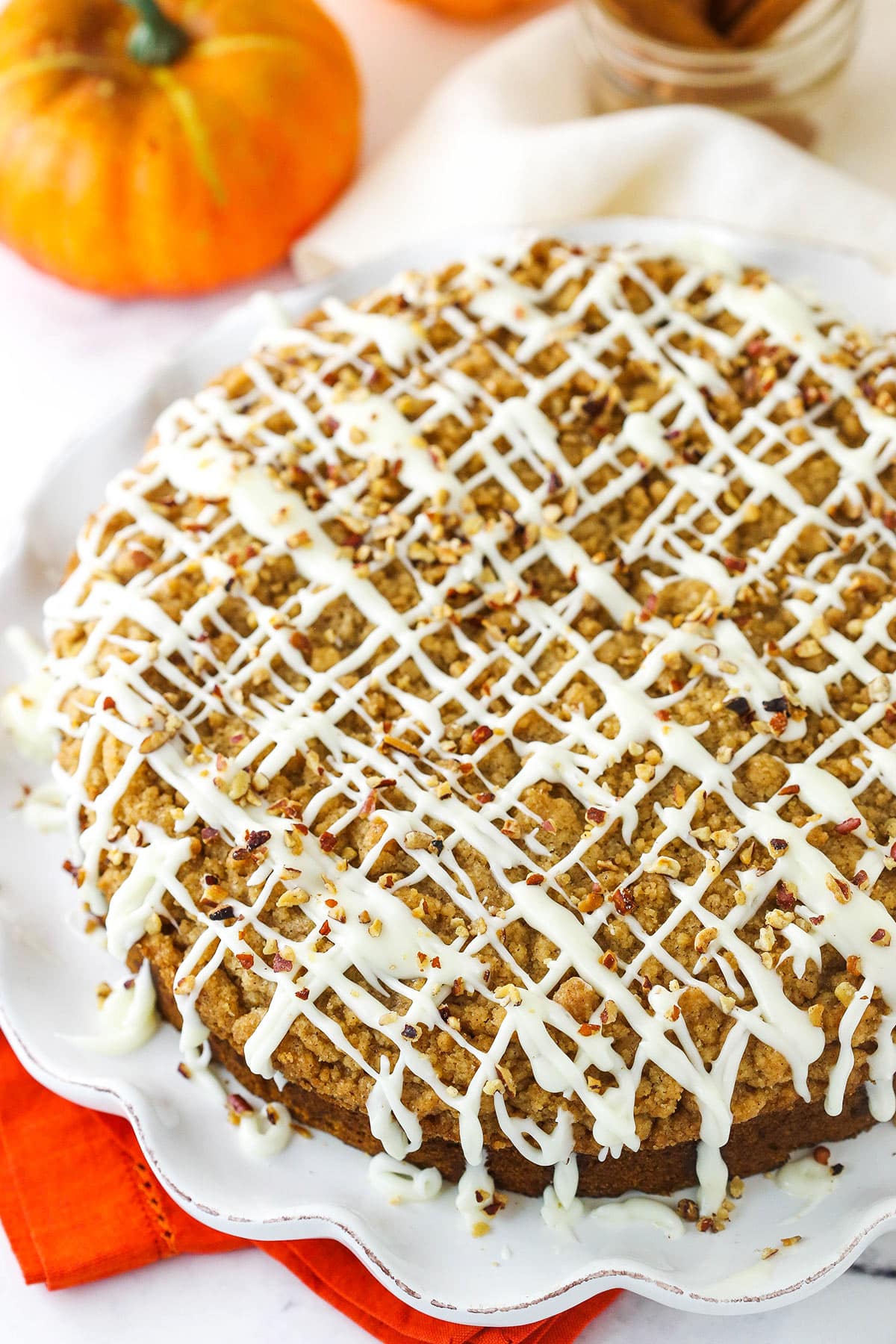 An uncut cinnamon streusel pumpkin coffee cake on a serving platter beside a small pumpkin