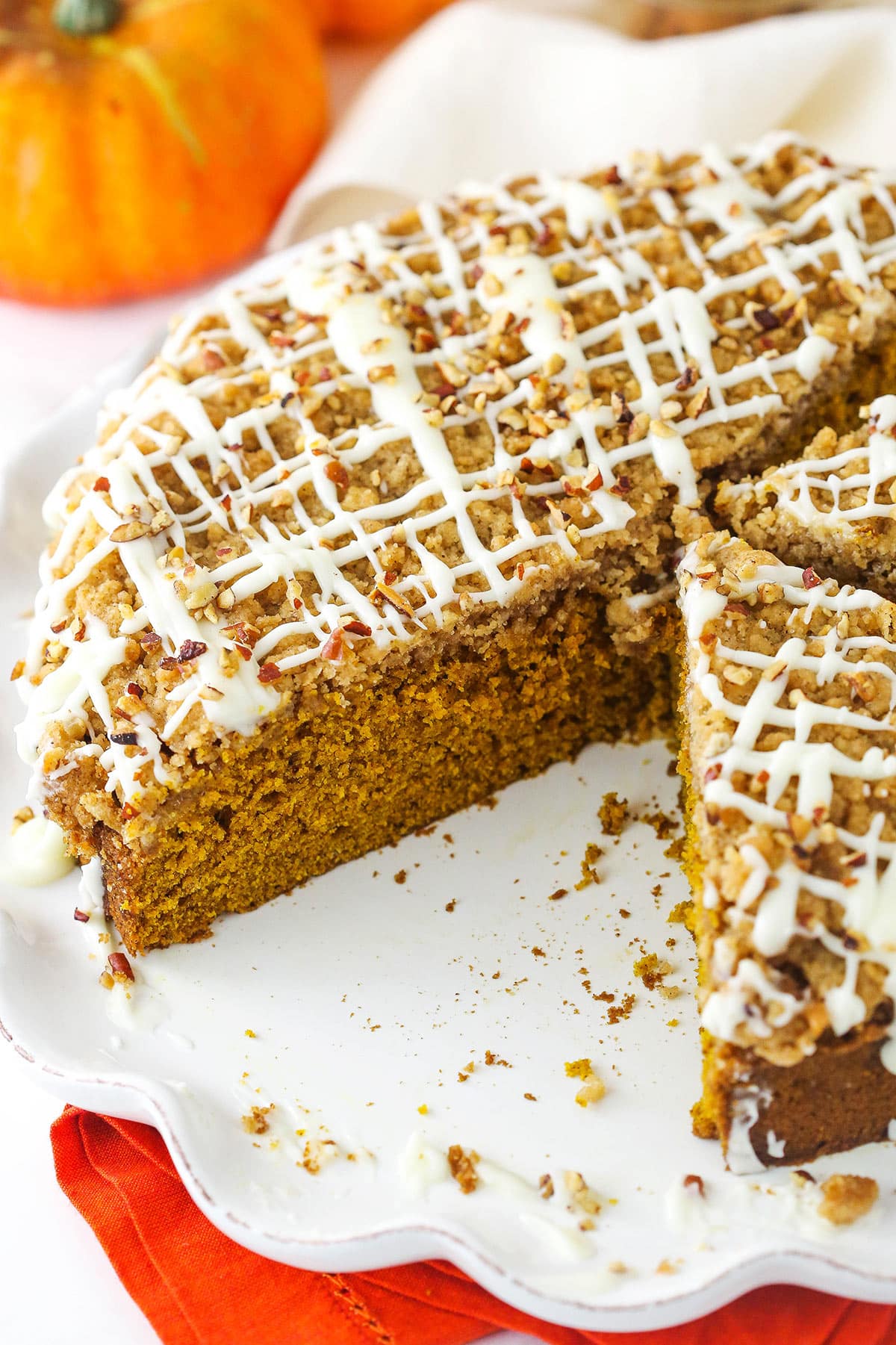 A cinnamon streusel coffee cake on a cake platter with one big slice missing.