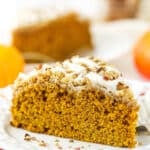 A slice of pumpkin coffee cake on a plate with a second slice and a jar of cinnamon sticks in the background