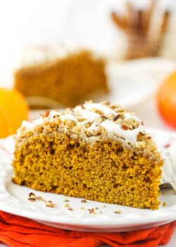 A slice of pumpkin coffee cake on a plate with a second slice and a jar of cinnamon sticks in the background