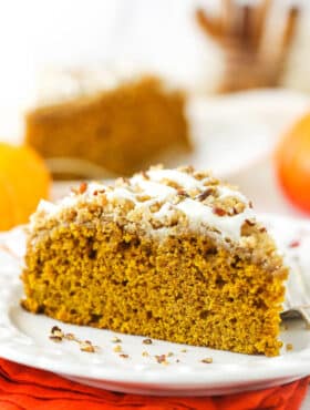 A slice of pumpkin coffee cake on a plate with a second slice and a jar of cinnamon sticks in the background