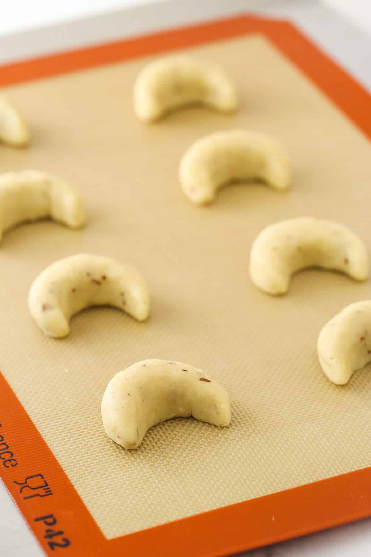 Shaping cookie dough into crescent shapes on a silicone baking mat.