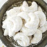 Almond crescent cookies dusted in powdered sugar on a plate.