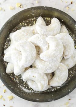 Almond crescent cookies dusted in powdered sugar on a plate.