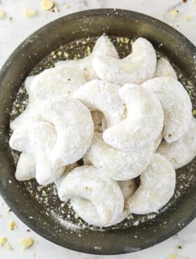 Almond crescent cookies dusted in powdered sugar on a plate.