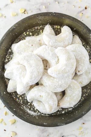 Almond crescent cookies dusted in powdered sugar on a plate.