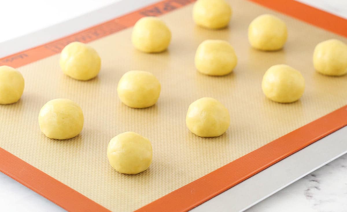 Anise cookie dough rolled into balls on a cookie tray lined with a silicone baking mat.