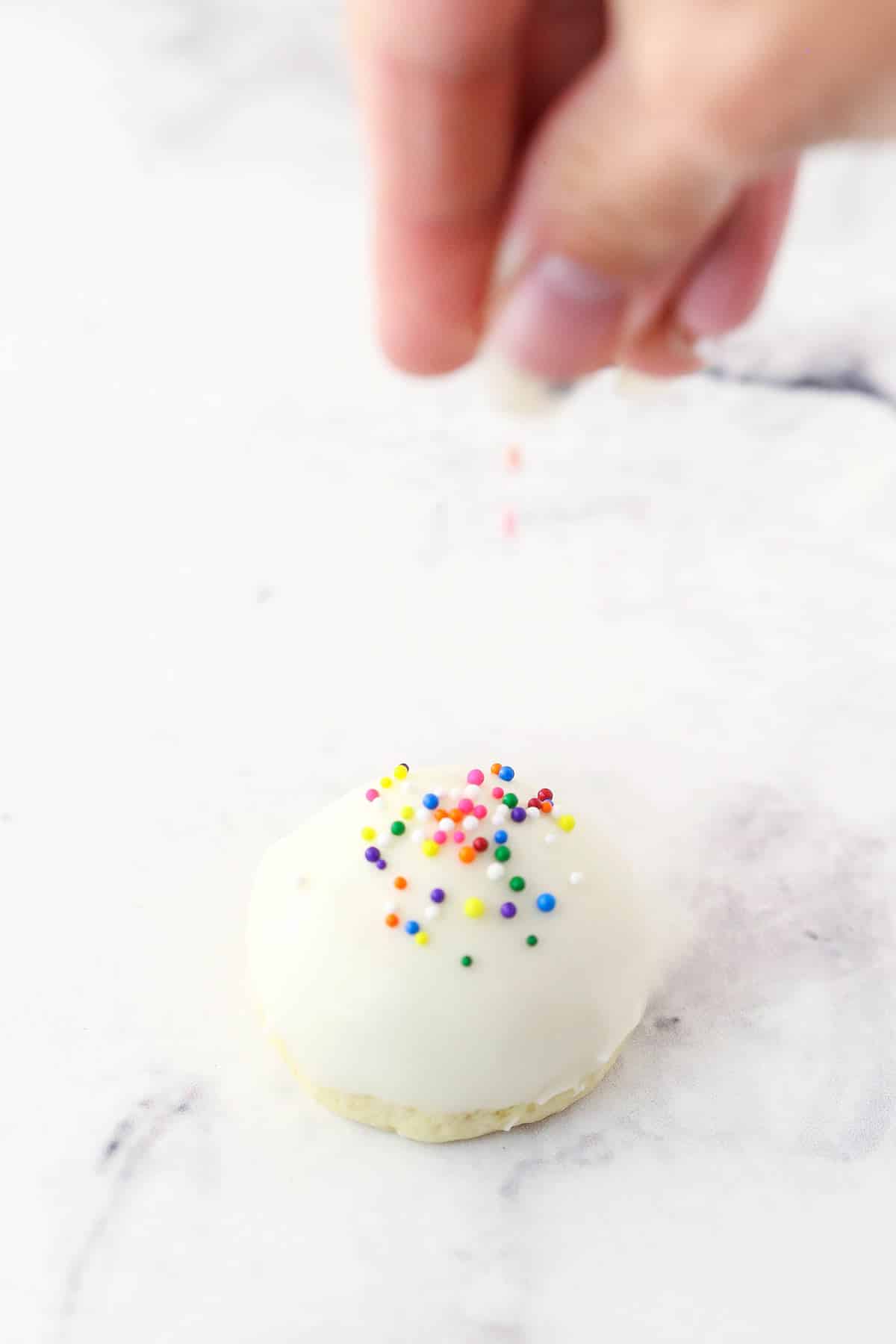 Putting colorful sprinkles on the top of iced anise cookies