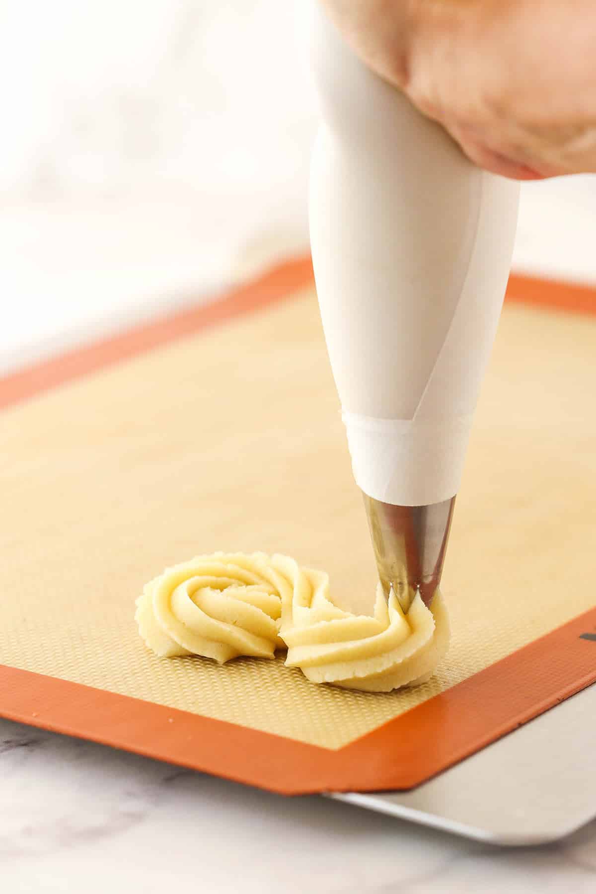 Piping spritz cookies on a silicone baking mat