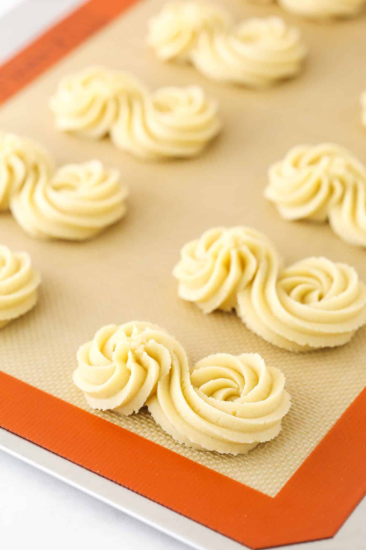 Piped spritz cookie dough in s-shapes on a silicone baking mat.