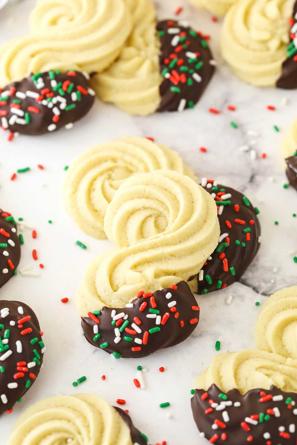 Spritz cookies dipped in chocolate and decorated with colorful sprinkles