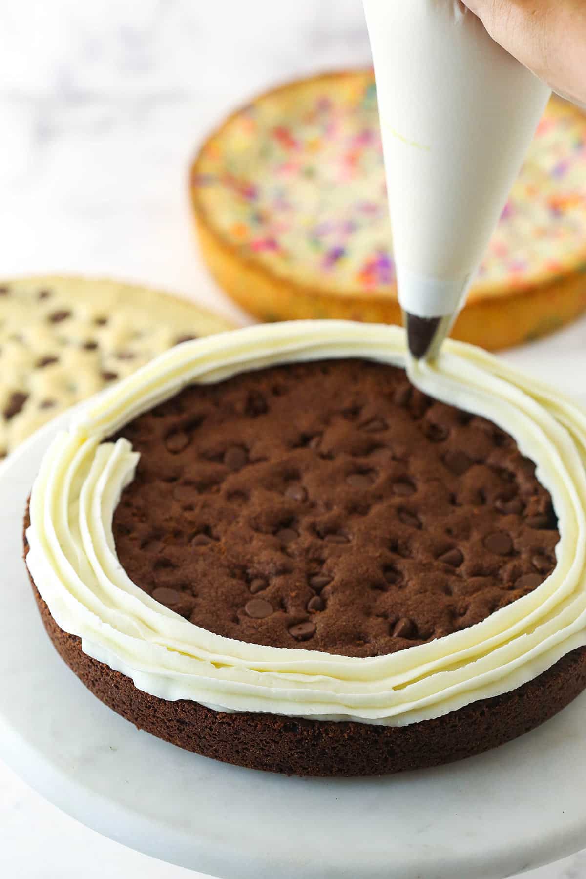 image showing the buttercream being piped onto the top of the double chocolate chip cookie cake
