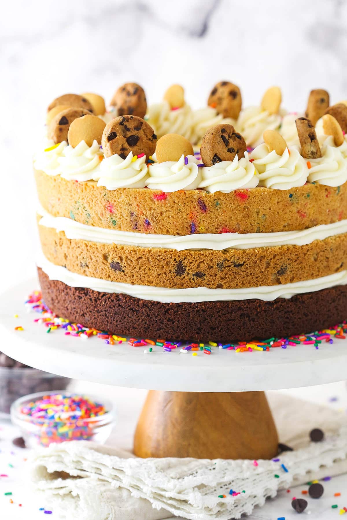 A triple-decker cookie cake sitting on a cake stand in front of a marble backdrop