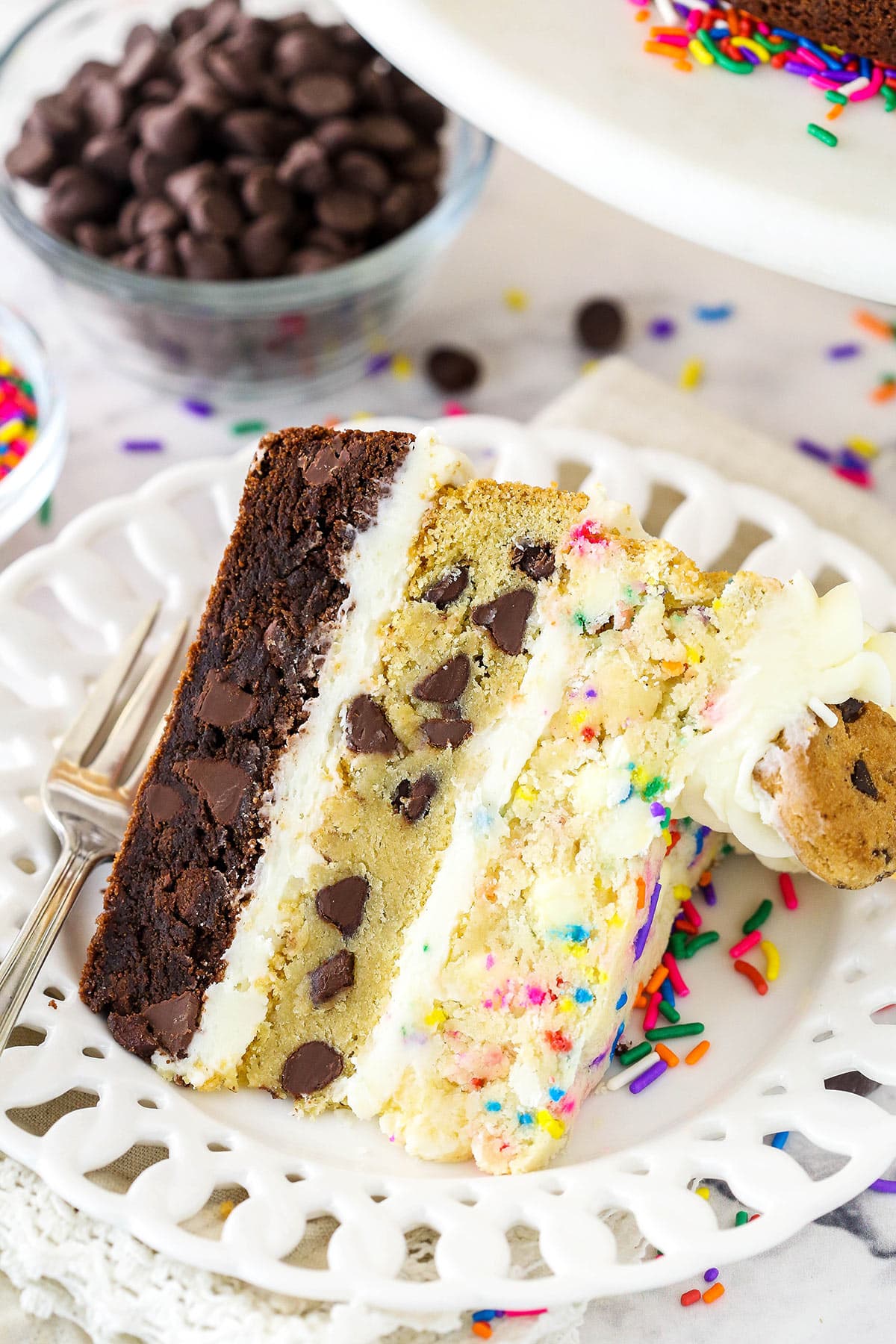 A slice of cookie cake on a plate with a bowl of chocolate chips and the remaining cake in the background