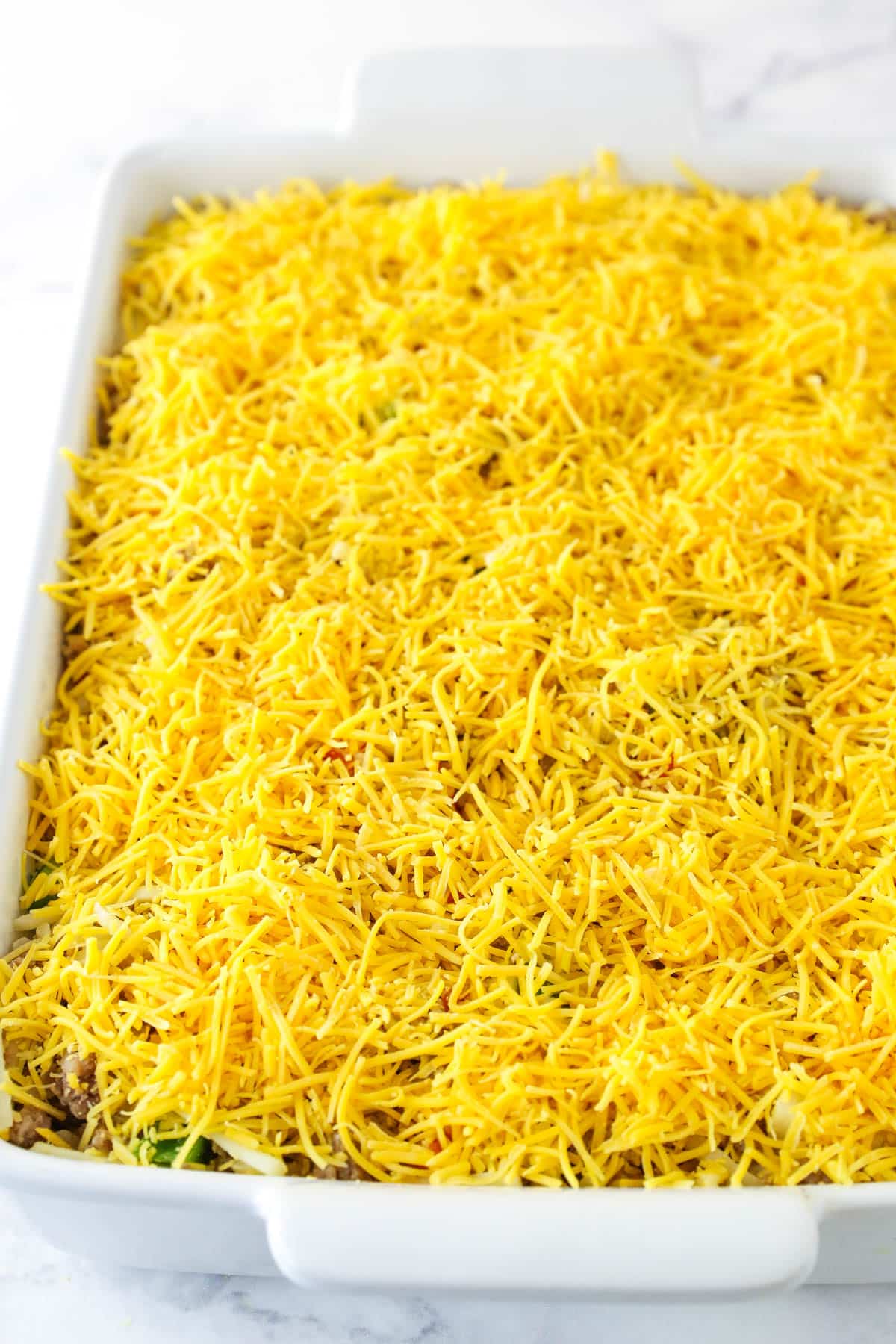 A layer of cheddar on top of the breakfast casserole - ready for baking