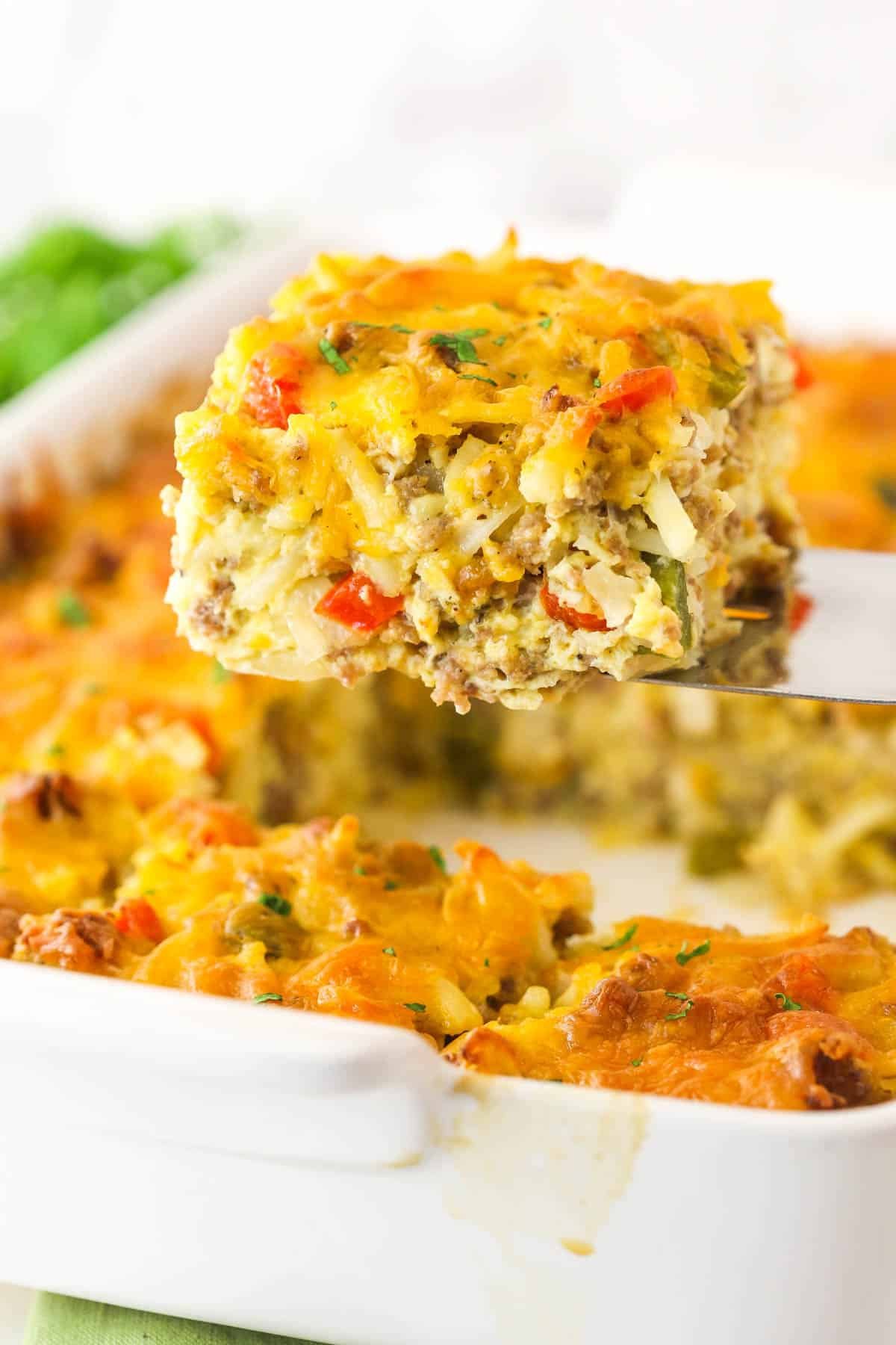 This Hashbrown Breakfast Casserole is perfect when you need to feed a crowd in the morning. Perfect for Christmas, Thanksgiving, or brunch! A piece of hashbrown breakfast casserole being lifted out of the baking dish