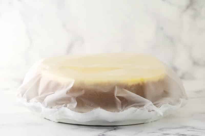 a cheesecake on a platter covered in plastic wrap on marble background