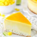 slice of mango key lime cheesecake on white plate with mango and limes in the background